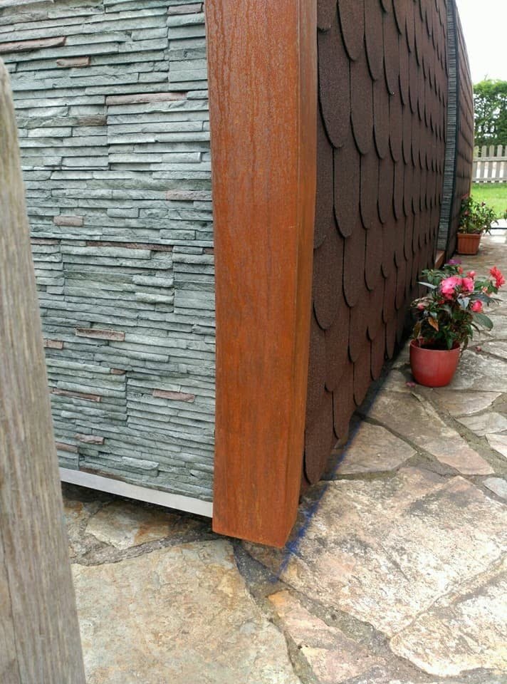 Detalle de materiales: piedra pizarra, acero Corten y tejado de escamas
