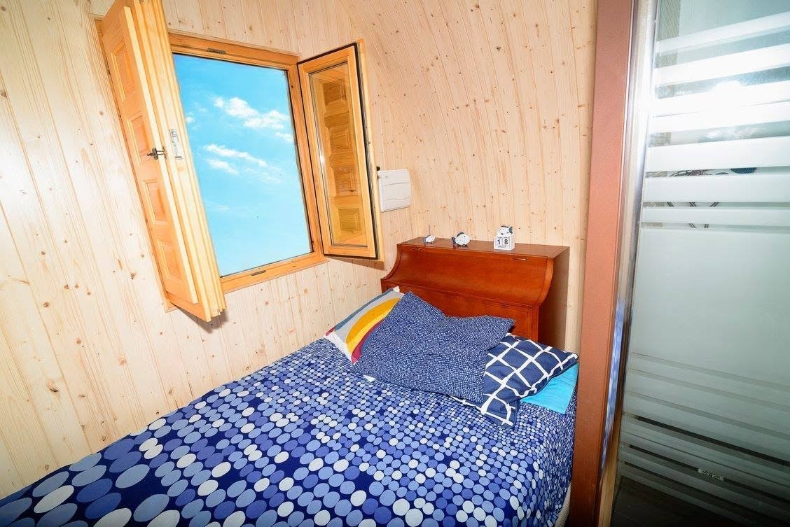 Dormitorio de Maxicozy con cama doble, ventana practicable y panelado de madera